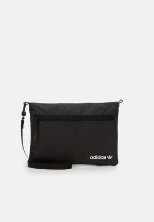 Zwart adidas polszakje met voorvak met rits, afneembare band en wit adidas-logo in de linkerbenedenhoek.