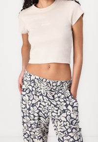 Korte beige geribbelde crop top met kapmouwen en wit logo. Gecombineerd met loszittende marineblauwe broek met bloemmotieven in het wit.