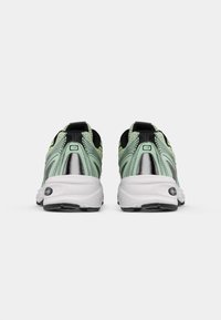 Sportschoenen met een mintgroene en zwarte mesh bovenkant, reflecterende zilveren accenten en een witte zool; heeft een gewatteerde kraag en textuurdetails.