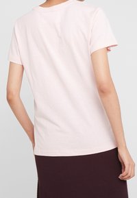 Ljust rosa bomullströja med rund halsringning och korta ärmar, har en avslappnad passform och mjuk textur. Synlig sömdetalj under midjan.