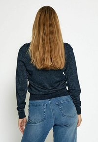 Granatowy sweter dzianinowy z błyszczącą fakturą, z ściągaczami na mankietach i u dołu. Noszony z jasnoniebieskimi dżinsami, posiadającymi tylne kieszenie i wyblakłe wykończenie.