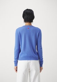 Blauer Pullover aus weichem Material, mit Rundhalsausschnitt, gerippten Bündchen und Saum sowie einem kleinen roten Herzdetail auf der Rückseite.