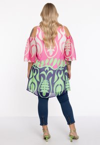 Leichte, durchsichtige Bluse mit pinken und grünen Blumenmustern, schulterfrei, kombiniert mit dunklen Jeans und grünen Absatzsandalen.
