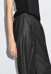 Zwarte streepjesslaap met een elastische tailleband, met een losse pasvorm en zachte textuur. Hand versierd met meerdere zilveren ringen.