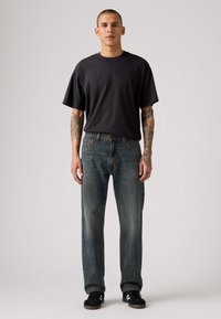 Camiseta oversized de algodón negra combinada con jeans de mezclilla azul desvaído. Los jeans tienen ligero desgaste y un corte recto. Zapatillas negras con acentos blancos.