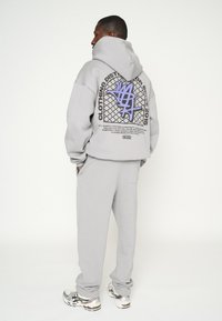 Sudadera gris con capucha y un gran gráfico en la parte posterior, combinada con pantalones de chándal grises a juego. La tela parece suave y tiene un corte relajado.