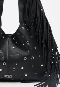 Czarna skórzana torba typu tote z detalem z frędzli, srebrnymi przelotkami i tłoczonym logo. Charakteryzuje się zakrzywionym górnym brzegiem i teksturowanym wykończeniem.