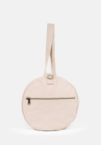 Round beige canvas bag with a textured finish, featuring a top loop, a flat shoulder strap, and a zippered pocket on the back.