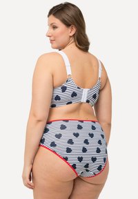 Páskovaný bikini set s námořnickými srdíčky, červenými akcenty a bílými popruhy. Obsahuje strukturovaný vršek s podprsenkou a design s vysokým pasem pro spodní díl.