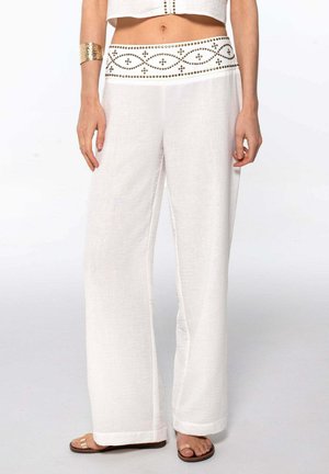 Pantalones de lino blancos de pierna ancha con una cinturilla decorativa con un patrón que presenta pequeños acentos dorados. Textura suave con un ajuste relajado.