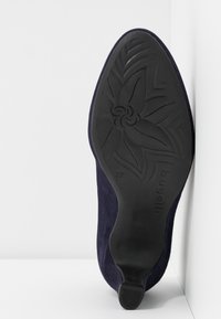 Semelle d'une chaussure à talon bleu marine montrant un motif floral, taille 37, et le nom de la marque "bugatti" sur une semelle en caoutchouc noir.