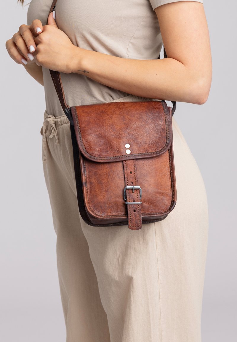 Brązowa skórzana torebka crossbody z przednią klapą, srebrnymi dodatkami i regulowanym paskiem. Teksturowana powierzchnia z polerowanym wykończeniem.