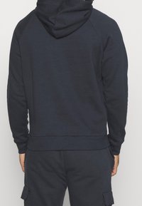 Sweat à capuche bleu marine en tissu doux, avec une capuche, des manches raglan et un ourlet côtelé. Conçu pour le confort avec une coupe décontractée.
