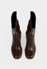 Paire de bottes mi-mollet en cuir marron foncé avec bouts carrés et détails de coutures, vues de dessus sur un fond uni.
