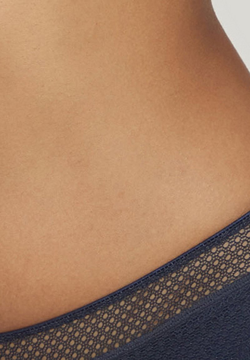 Granatowy materiał z teksturowanym, otwartym siateczkowym akcentem wzdłuż górnej krawędzi. Gładka skóra o kolorze naturalnym widoczna poniżej siateczki.