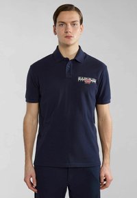 Tummansininen polo-paita puuvillamateriaalista, jossa on kahden napin helma, lyhyet hihat ja logo vasemmassa rinnassa.