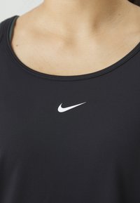 Svart atletisk tanktopp med rund halslinje. Har et hvitt Nike swoosh-logo i midten. Glatt, elastisk tekstur.