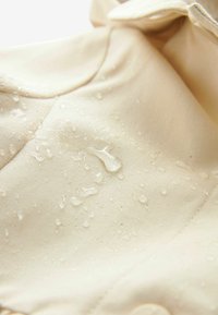 Tissu beige avec des gouttelettes d'eau visibles, présentant une texture lisse et un détail de bouton, indiquant des propriétés résistantes à l'eau.