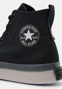Schwarze Stoff-Hochtop-Sneaker mit Gummisohle, ausgestattet mit einem runden Logo-Patch mit einem Stern und dem Text "Converse All Star".