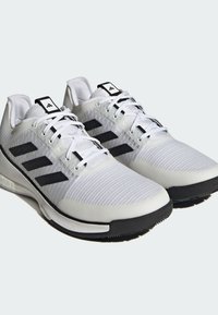 Weiße Sportschuhe mit einem strukturierten Obermaterial, schwarzem Drei-Streifen-Design und schwarzem Außensohlen. Die Schnürsenkel und die Zunge sind weiß.