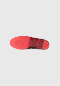 Brown leather shoe sole with a bright red rubber bottom, engraved logo, and embossed detailing. Flat shape with a slight arch design.