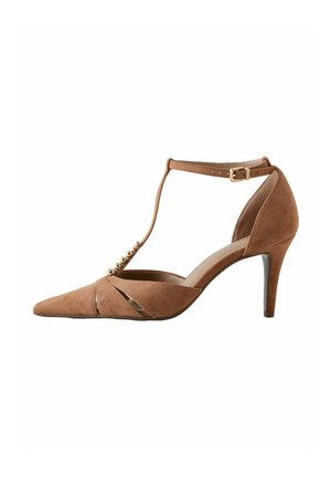 Hnědá semišová lodička na vysokém podpatku s bodatou špičkou, T-popruh ozdobený zlatými korálky, přezka u kotníku a středně vysoký jehlový podpatek.