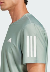 Camiseta atlética de color verde claro con textura de malla, mangas cortas y el logotipo blanco de Adidas en el pecho, además de tres franjas en el hombro.