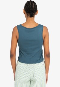 Afskåret teal tanktop med en glat tekstur og rund udskæring, parret med grønstribede brede bukser med sidelommer.