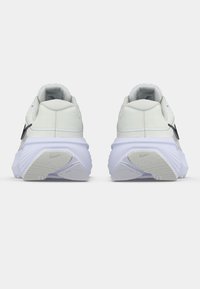 Λευκά αθλητικά παπούτσια με υφασμάτινη πάνω επιφάνεια με υφή, μαλακή κολόνα και παχιά λευκή ενδιάμεση σόλα, με εμφανές μαύρο λογότυπο στο πλάι κάθε παπουτσιού.