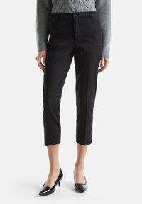 Czarne rybaczki o gładkiej fakturze, z frontowym zapięciem na guzik, szlufkami na pasek oraz dopasowanym krojem. W połączeniu z błyszczącymi szpilkami.