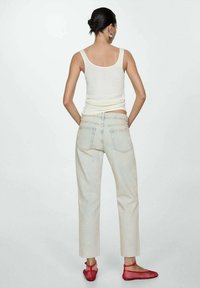 Jeans rectos de color beige claro con un dobladillo ligeramente cortado, combinados con una camiseta ajustada blanca y zapatos planos de malla rojos.