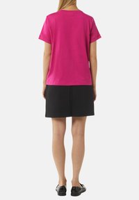 Fuchsia Baumwoll-T-Shirt mit kurzen Ärmeln, Rundhalsausschnitt und lockerer Passform, kombiniert mit einem schwarzen strukturierten Rock und schwarzen Schuhen.