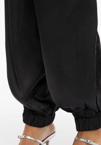 Czarne aksamitne spodnie dresowe ze ściągaczami przy nogawkach, o gładkiej fakturze i luźnym kroju. Połączone z srebrnymi sandałami na paski.