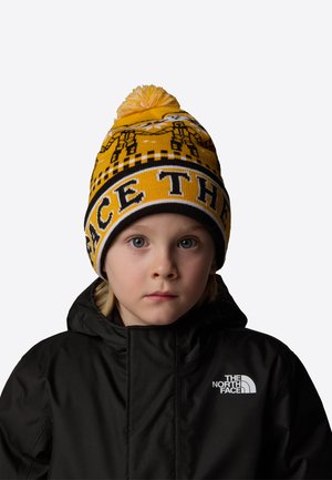 Żółta dzianinowa czapka z wzorem i pomponem na górze, z czarnymi akcentami oraz nadrukiem "THE NORTH FACE" dużymi literami.