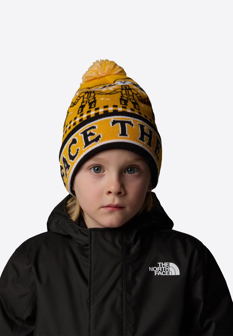 Żółta dzianinowa czapka z wzorem i pomponem na górze, z czarnymi akcentami oraz nadrukiem "THE NORTH FACE" dużymi literami.