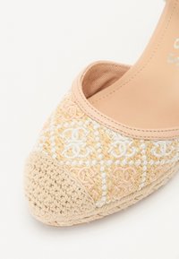 Vevd stoff sko med avrundet tå, med beige og lyserøde broderimønstre, og en teksturert heklet såle.