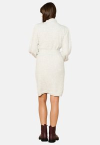 White textured wrap dress with long sleeves, belt at the waist, and a diamond pattern. Paired with maroon ankle boots.