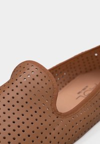 Καφέ παπούτσι τύπου slip-on με ομοιόμορφες στρογγυλές οπές και λείo χείλος γύρω από το άνοιγμα, απεικονίζεται σε κοντινό πλάνο.