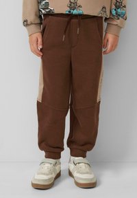 Braune Jogginghosen mit beiger Seitenpartie, elastischem Bund mit Kordelzug und gerippten Bündchen, aus weichem, strukturiertem Stoff gefertigt.
