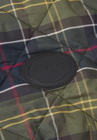 Tecido acolchoado com um padrão de xadrez verde e azul com linhas amarelas e vermelhas; inclui um emblema redondo em relevo com o logótipo da Barbour.
