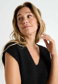 Pull noir à manches courtes avec un décolleté en V, fabriqué en tissu texturé doux. Il présente une coupe ample et un aspect doux.