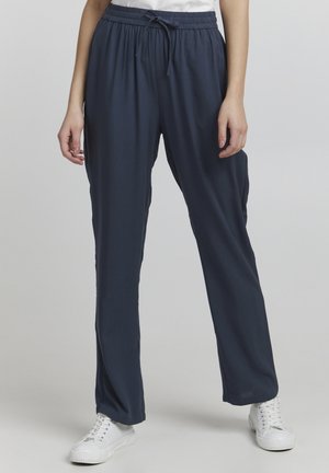 Navy pull-on pants with an elastic waistband and drawstring, featuring a relaxed fit and a smooth, lightweight fabric. Paired with white sneakers.