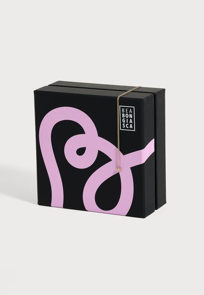 Boîte Bea Bongiasca noire et rose avec un collier en or présentant un petit pendentif abeille drapé sur le bord supérieur sur un fond blanc.