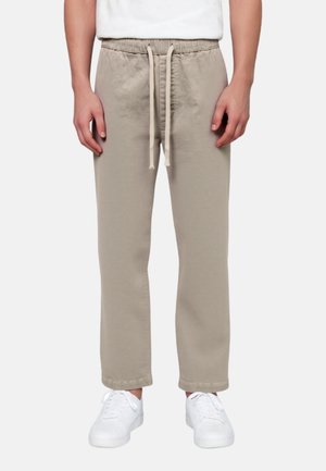 Pantalones beige con cordón, usados con zapatillas blancas, cortados por encima de los tobillos y combinados con una camisa blanca.