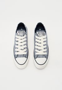 Une paire de baskets Converse All Star à carreaux bleu marine et blancs avec des lacets blancs et des embouts en caoutchouc, sur un fond blanc.