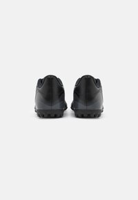 Chaussures de football noires avec une tige en cuir lisse, des accents texturés et une semelle en caoutchouc cloutée. Vue arrière montrant un design épuré et des coutures.