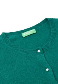 Zelený pletený kardigan s kulatým výstřihem, který má vpředu dva bílé knoflíky a štítek s nápisem "United Colors of Benetton".