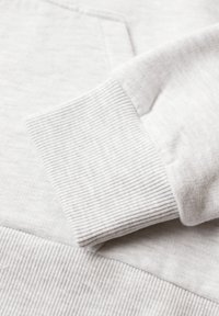 Pull blanc en tricot à manches longues avec poignets et ourlet côtelés, montrant la texture du tissu et les détails des coutures.