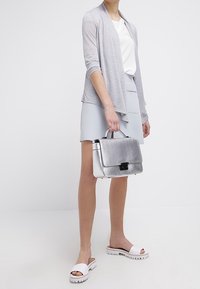 Srebrna metaliczna torebka na klapkę z czarnym okuciem, w zestawie z jasnoszarym kardiganem, białą bluzką, szarym spódnicą i białymi sandałami.
