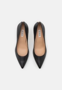 Escarpins noirs en cuir à bout pointu avec une finition lisse, arborant une doublure intérieure nude et un logo GUESS sur la semelle intérieure.